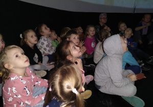 Dzieci siedzą wewnątrz kopuły i oglądają film.